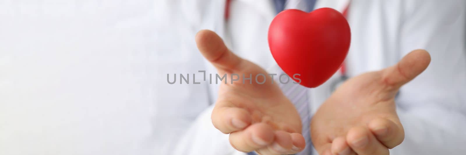 Doctor cardiologist holds hands and airborne red toy heart closeup. Cardiotherapist and treatment of heart diseases