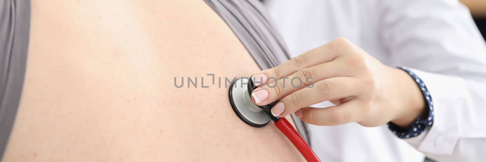 Female doctor listens to man back through astethoscope. Inflammation of lungs and painful cough