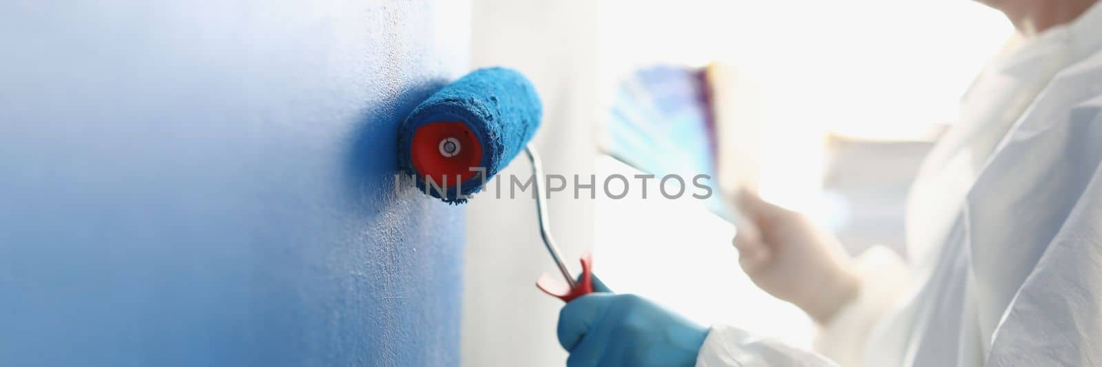 Painting white wall with blue roller. Services of master painter for home repair