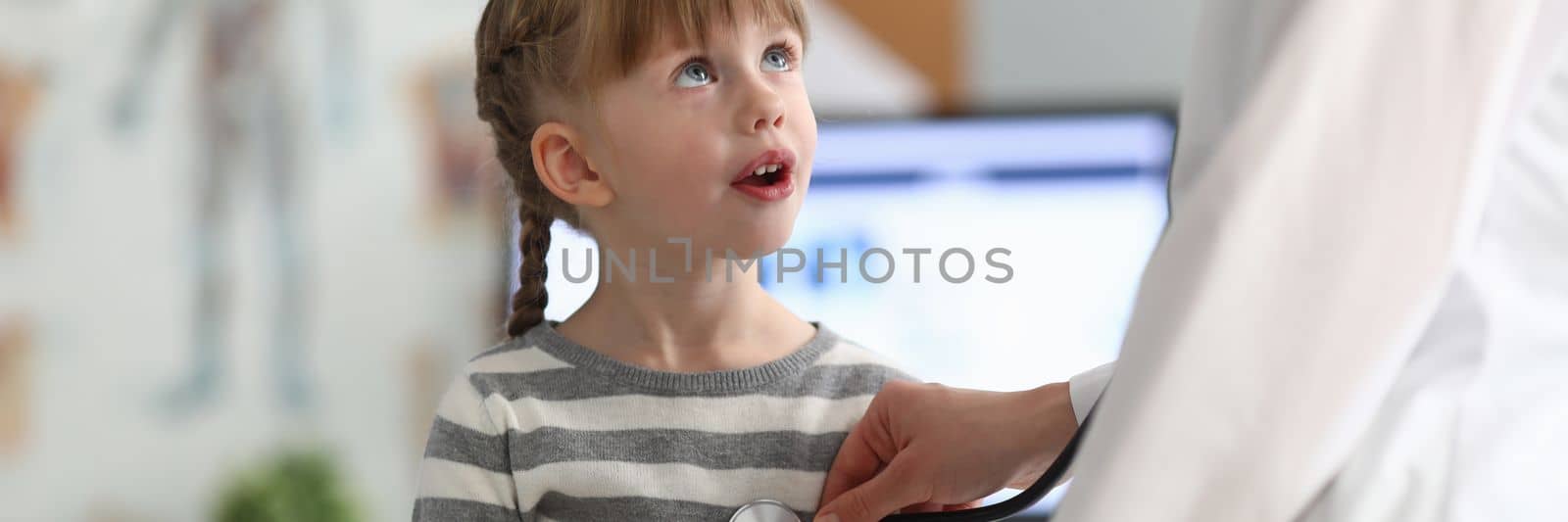 Smiling girl at doctor office in clinic. Female pediatrician examining small child with a stethoscope