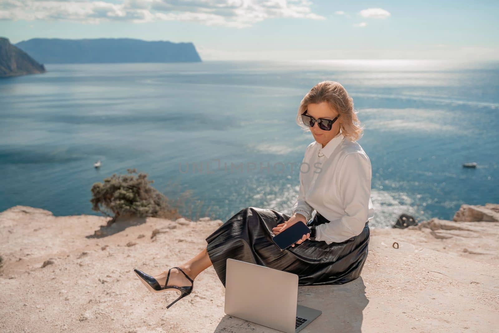 Freelance women sea. She is working on the computer. Good looking middle aged woman typing on a laptop keyboard outdoors with a beautiful sea view. The concept of remote work. by Matiunina