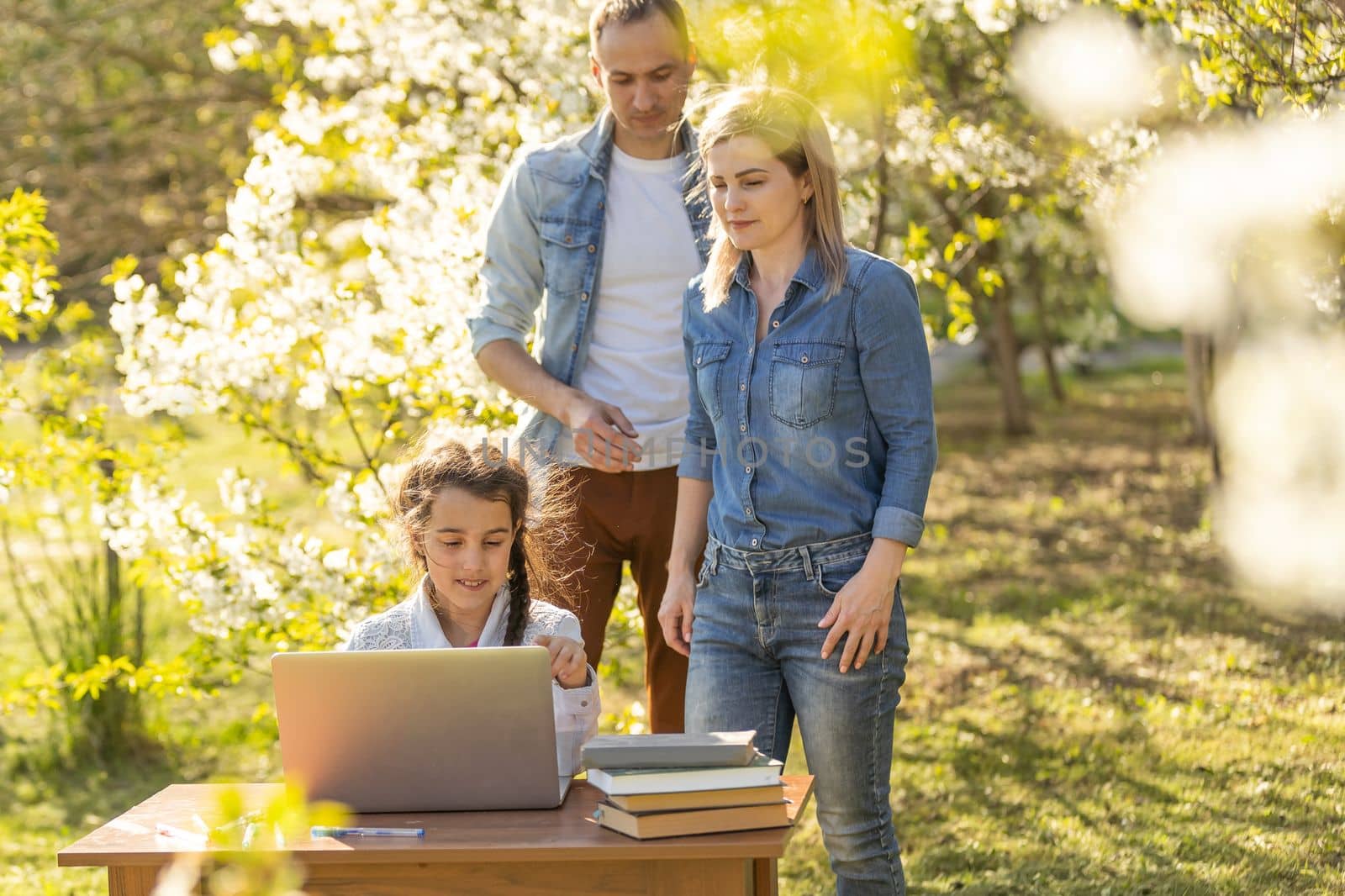 Happy family of four parents and cute little girl studying on laptop, enjoy using laptop watching cartoons, make internet video call or shopping online looking at computer screen sit together outdoor by Andelov13