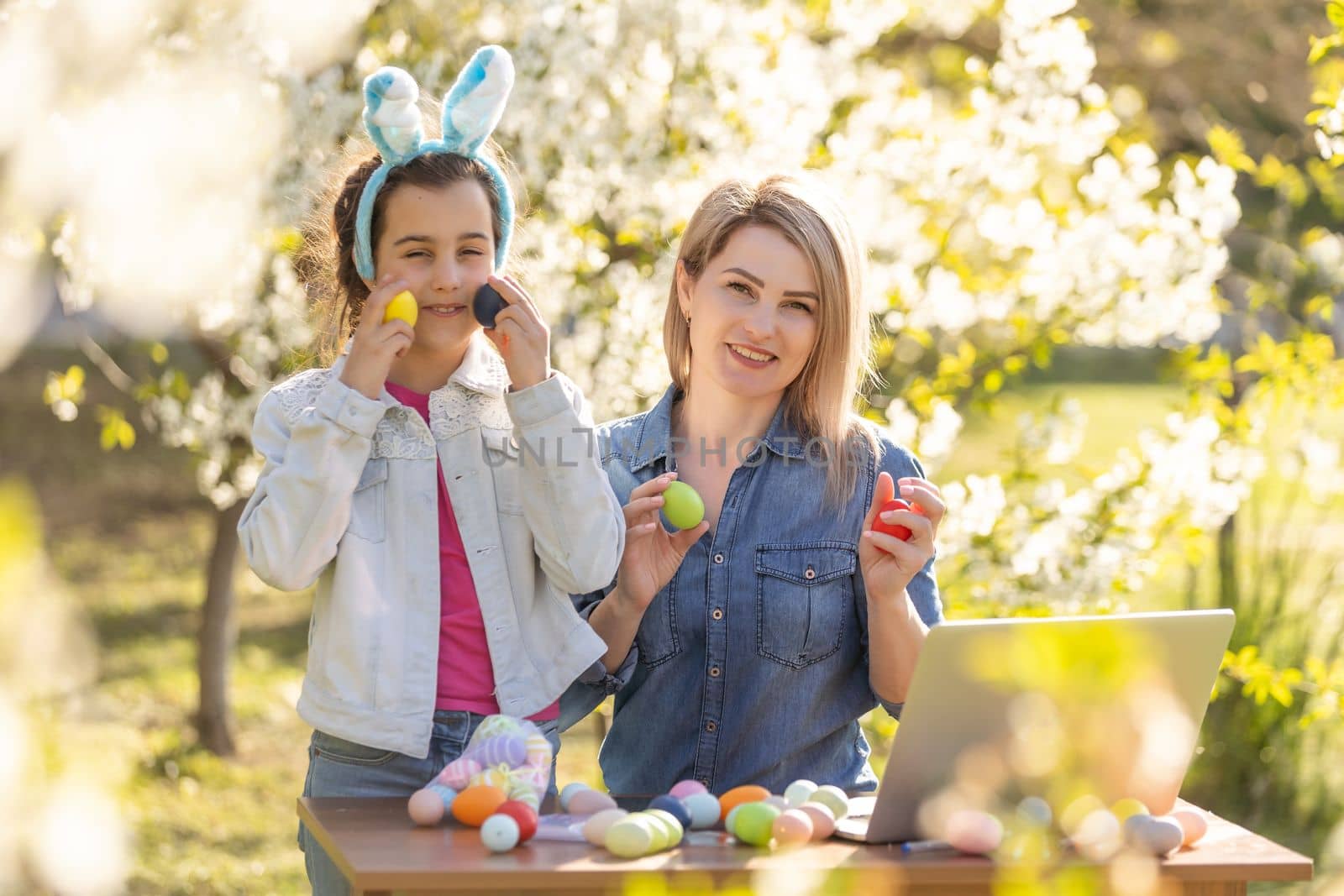 mother and daughter paint easter eggs with laptop, record lessons on a webcam with a laptop. mother and daughter are preparing for the holiday together