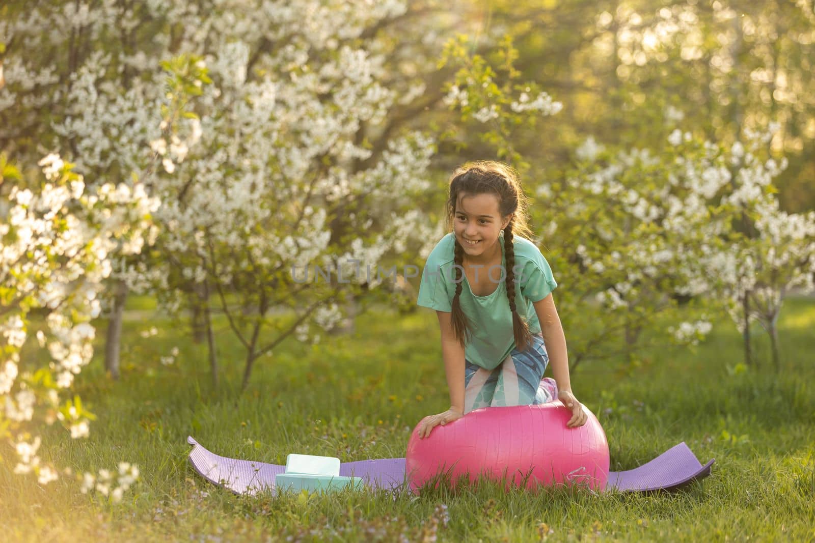 a little girl does yoga lying on a sports mat in the park. a healthy lifestyle is a childish habit by Andelov13