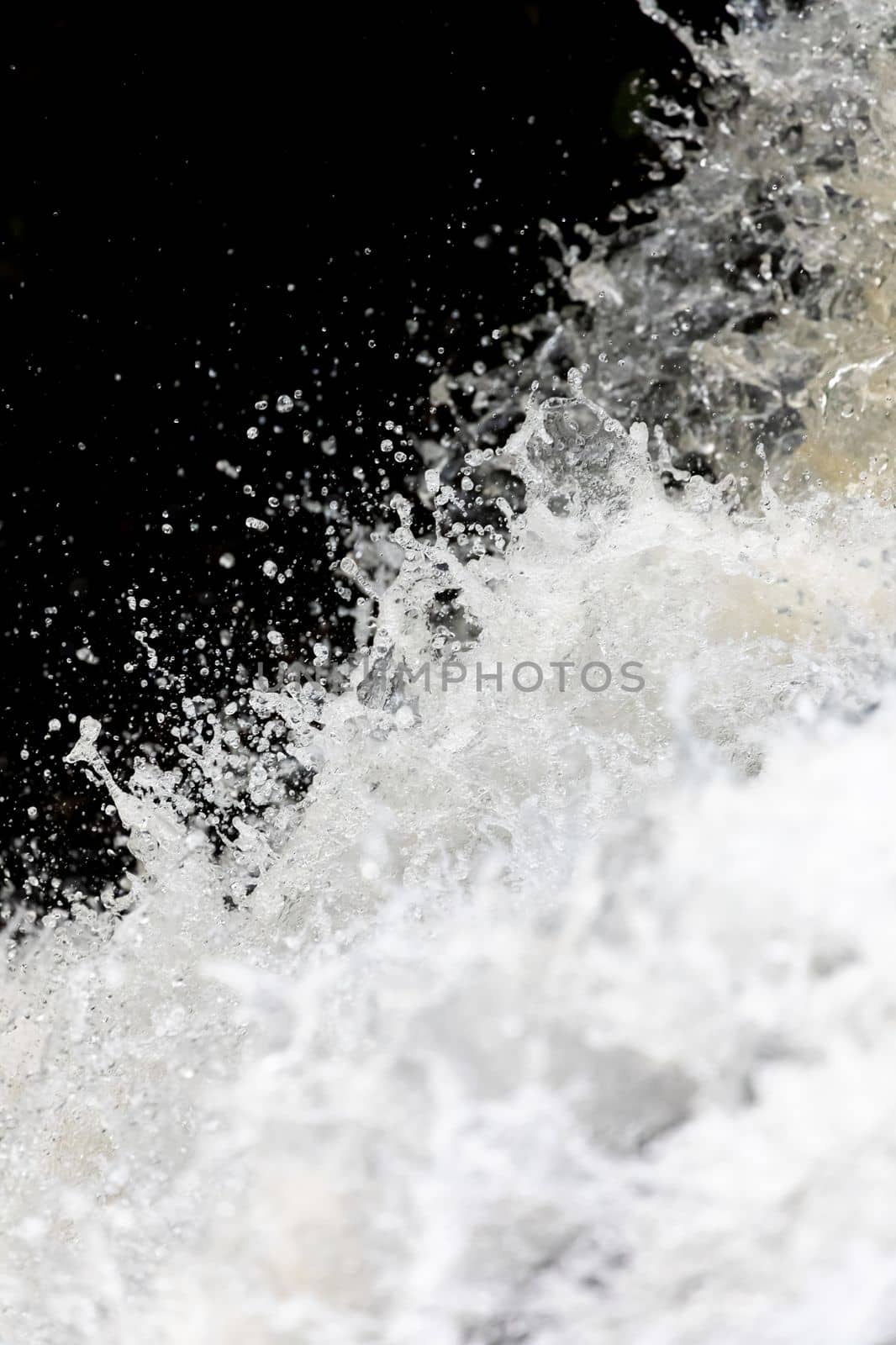 Close focus on splashing water of waterfall with dark background.