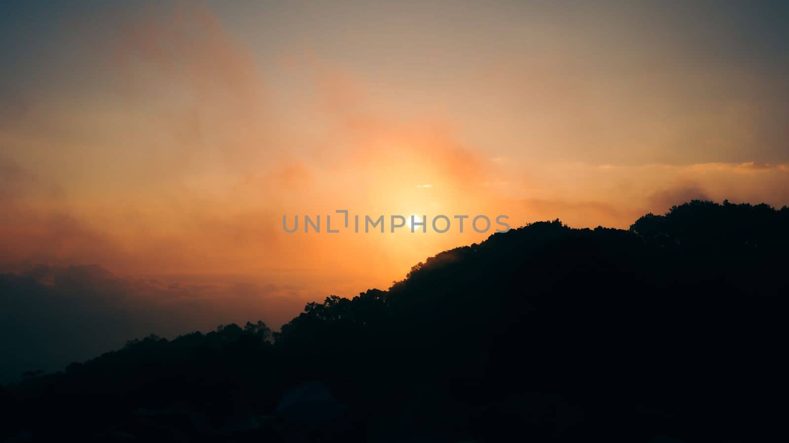 Aerial view of dramatic sunrise and cloudy sky over silhouetted mountain of tropical rainforest during winter season.