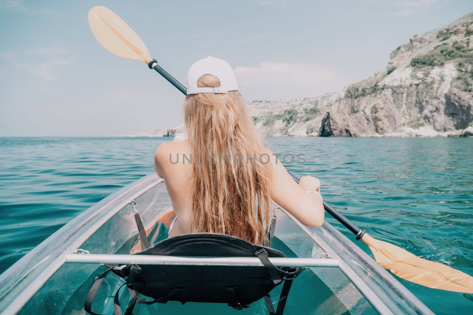 Woman in kayak back view. Happy young woman with long hair floating in transparent kayak on the crystal clear sea. Summer holiday vacation and cheerful female people relaxing having fun on the boat by panophotograph