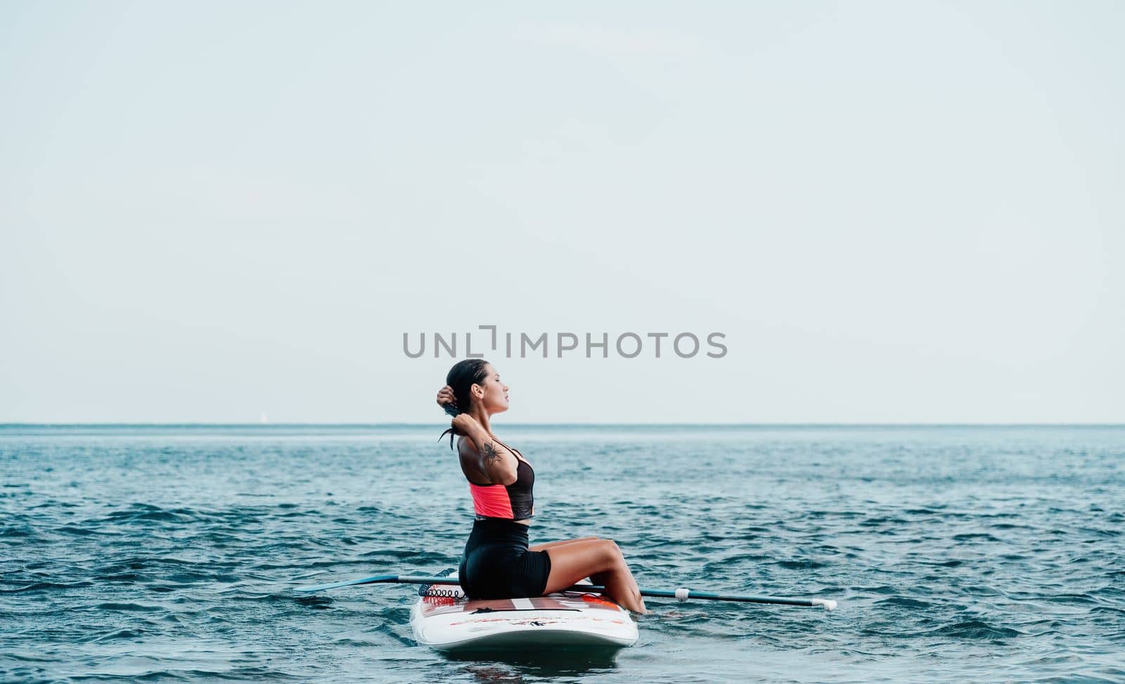 Sea woman sup. Silhouette of happy young woman in pink bikini, surfing on SUP board, confident paddling through water surface. Idyllic sunset. Active lifestyle at sea or river. by panophotograph