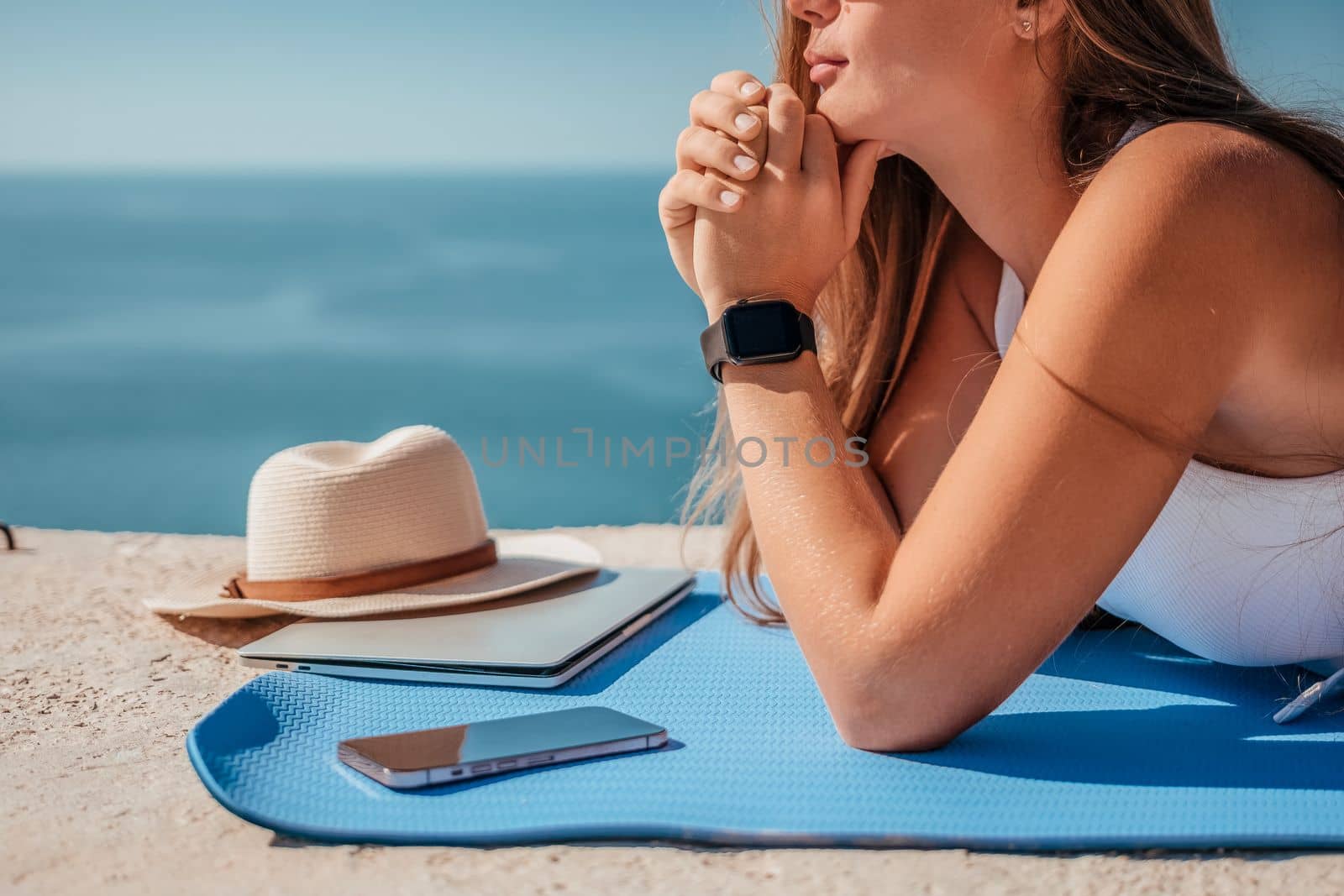 Digital nomad, woman in the hat, a business woman with a laptop sits on the rocks by the sea during sunset, makes a business transaction online from a distance. Freelance, remote work on vacation. by panophotograph