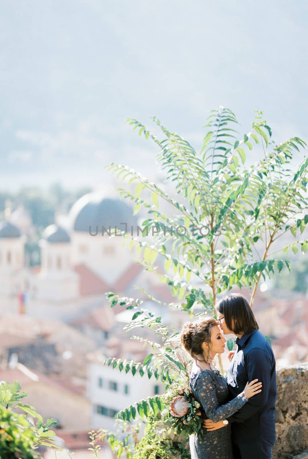 Groom kisses the forehead of bride in a blue dress on the observation deck over the city. High quality photo