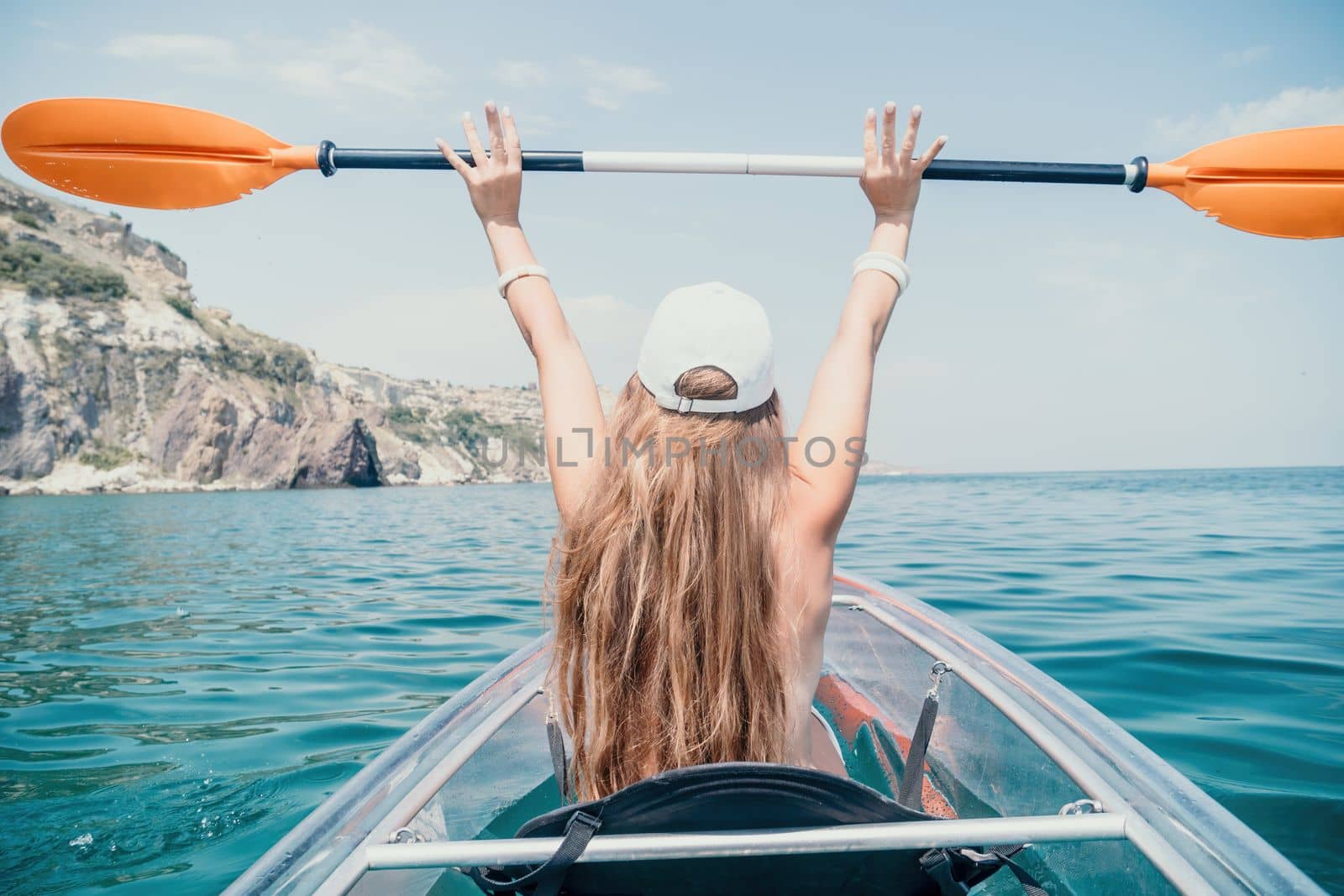 Woman in kayak back view. Happy young woman with long hair floating in transparent kayak on the crystal clear sea. Summer holiday vacation and cheerful female people having fun on the boat.