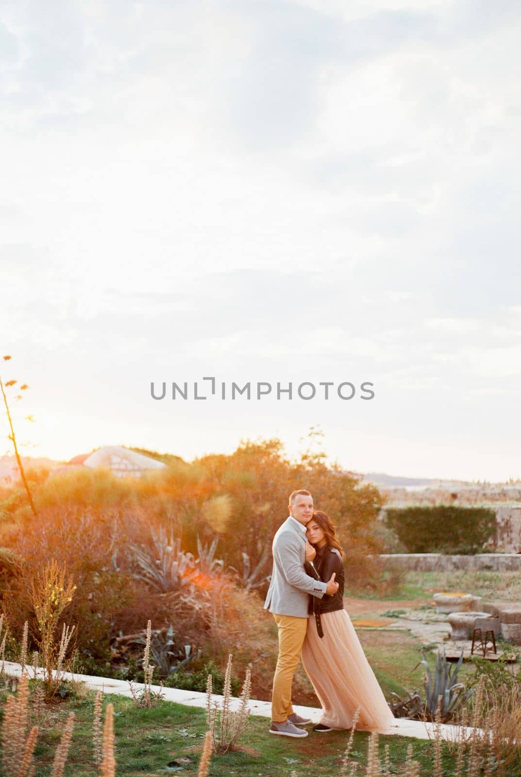 Groom hugging bride standing on stone path at sunset. High quality photo