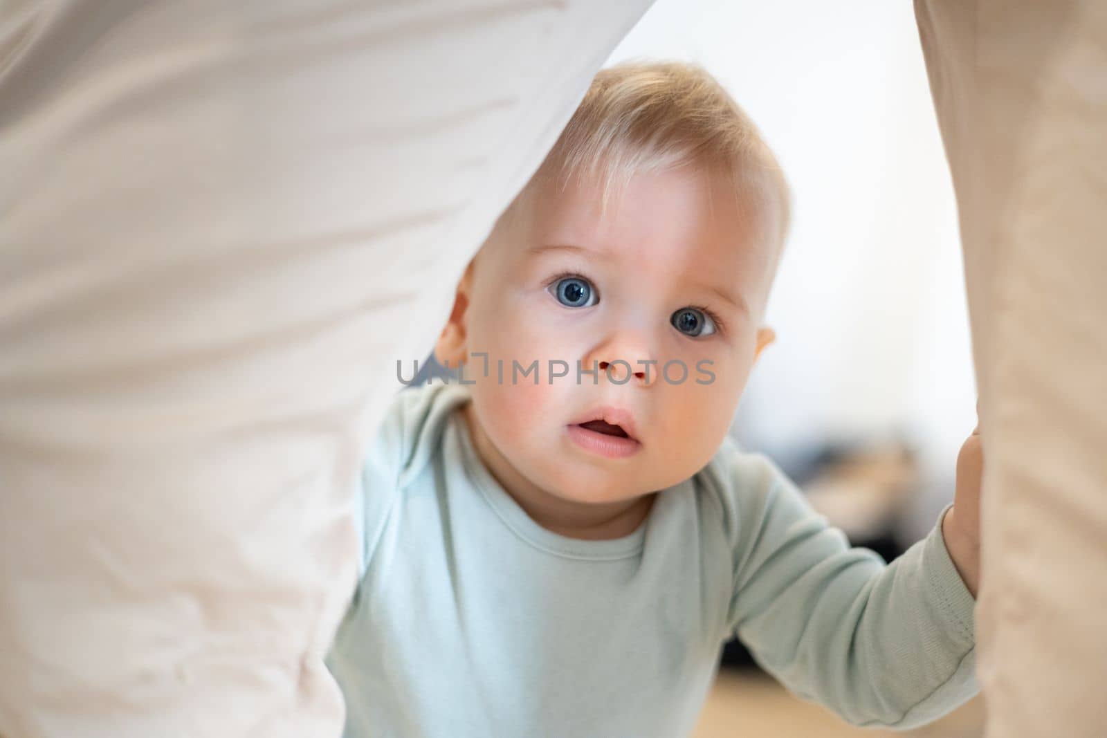 Portrait of adorable curious infant baby boy child taking first steps holding to father's pants at home. Cute baby boy learning to walk