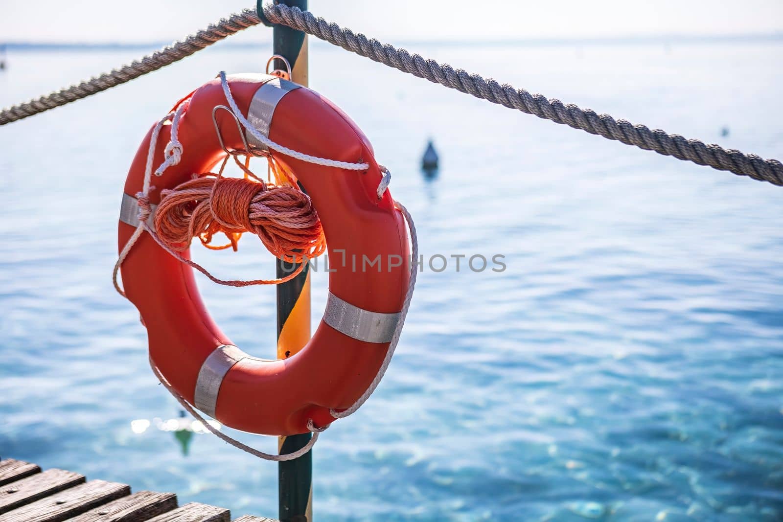 A red lifesaver on a wooden dock at Lake Garda, a popular tourist destination in Italy, symbolizing safety and security for water activities.