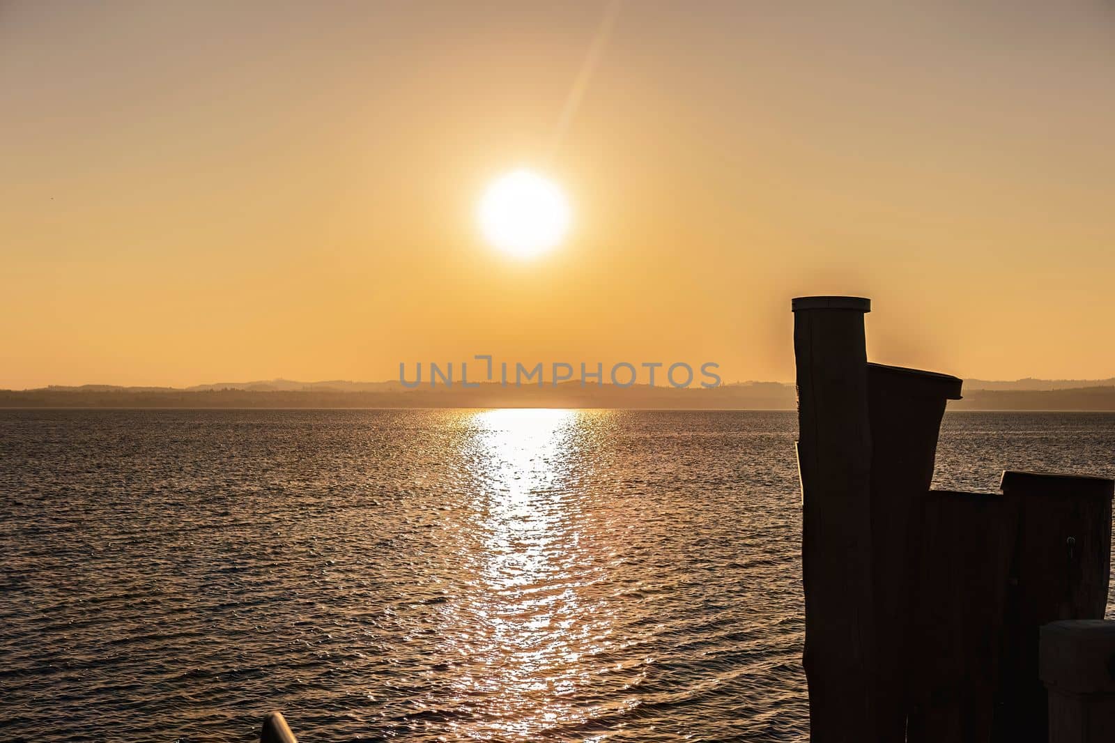 Beautiful sunset over the stunning Garda Lake in Italy, with the sun reflecting on the calm water and creating a peaceful atmosphere. Perfect for travel and nature-related projects.