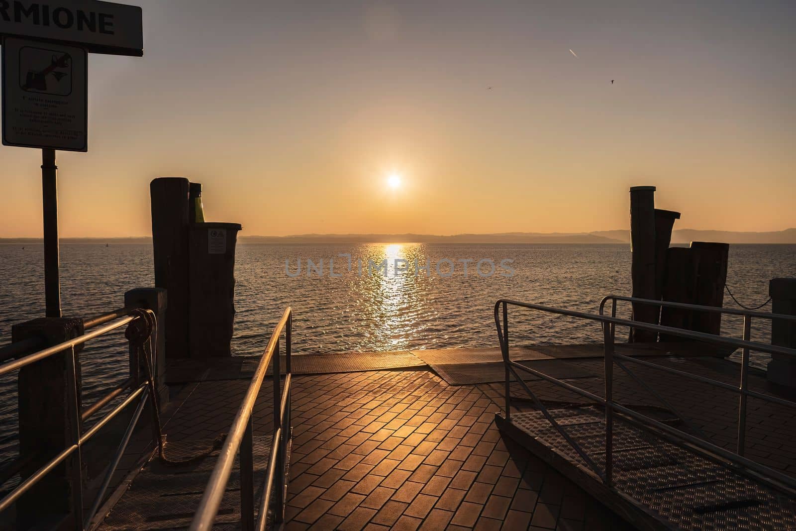 Beautiful sunset over the stunning Garda Lake in Italy, with the sun reflecting on the calm water and creating a peaceful atmosphere. Perfect for travel and nature-related projects.
