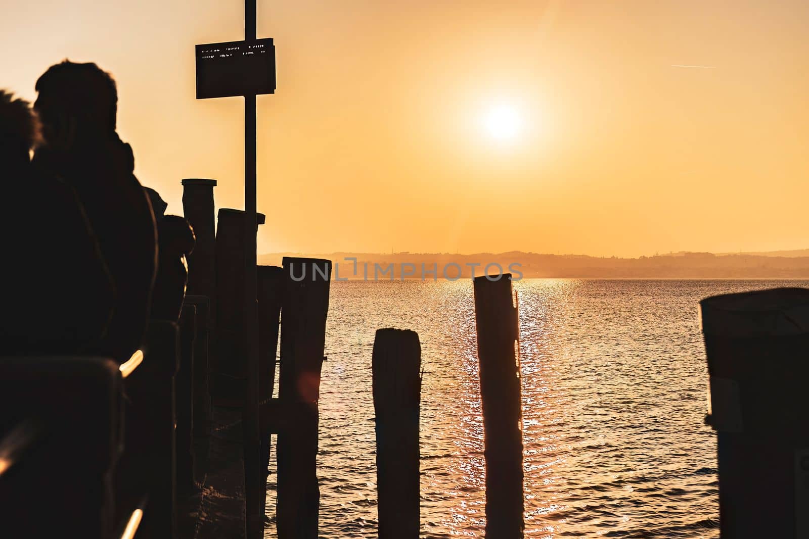 A group of people silhouetted against a beautiful sunset at Garda pier, Italy