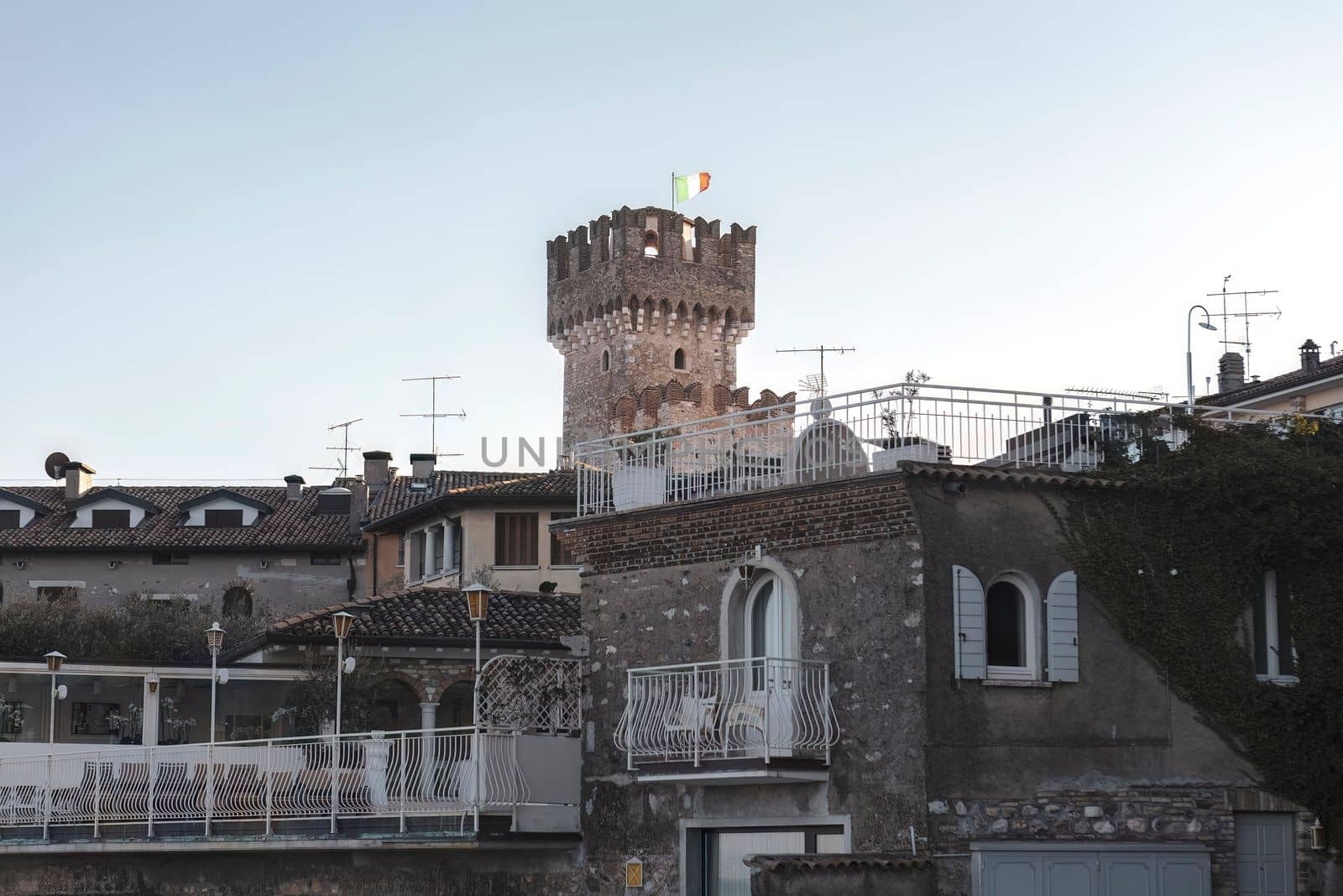 A stunning view of the castle in Sirmione, Italy, surrounded by the beautiful blue waters of Lake Garda. The ancient walls and towers of the castle create an impressive contrast against the blue sky by pippocarlot