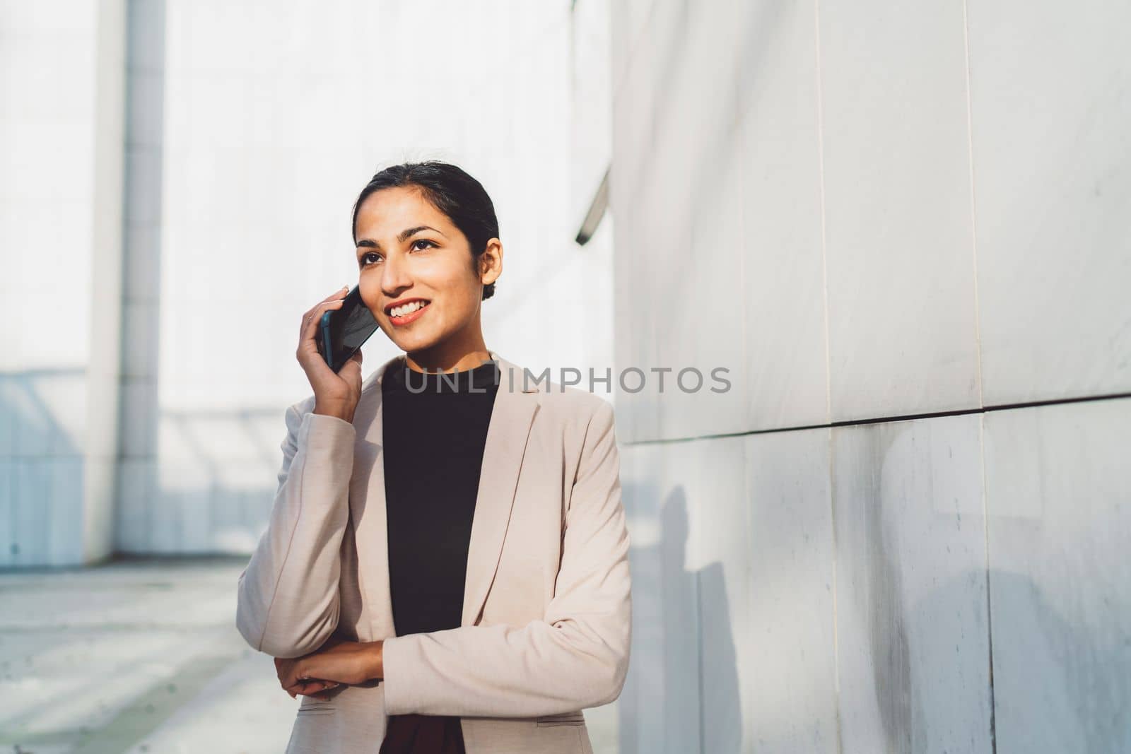 Young businesswoman walking outside while on her phone, talking to a friend on her lunch break. Business woman outside the office building on a sunny day.