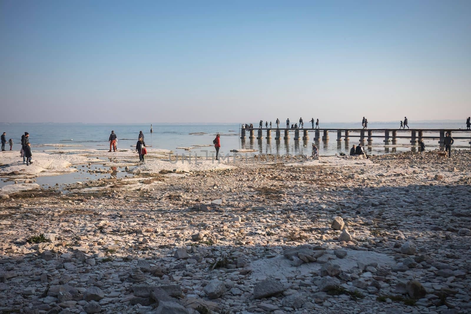 Sirmione, Italy 15 February 2023: A stunning landscape photo of a rocky beach in Sirmione, with the clear waters of Lake Garda in the background