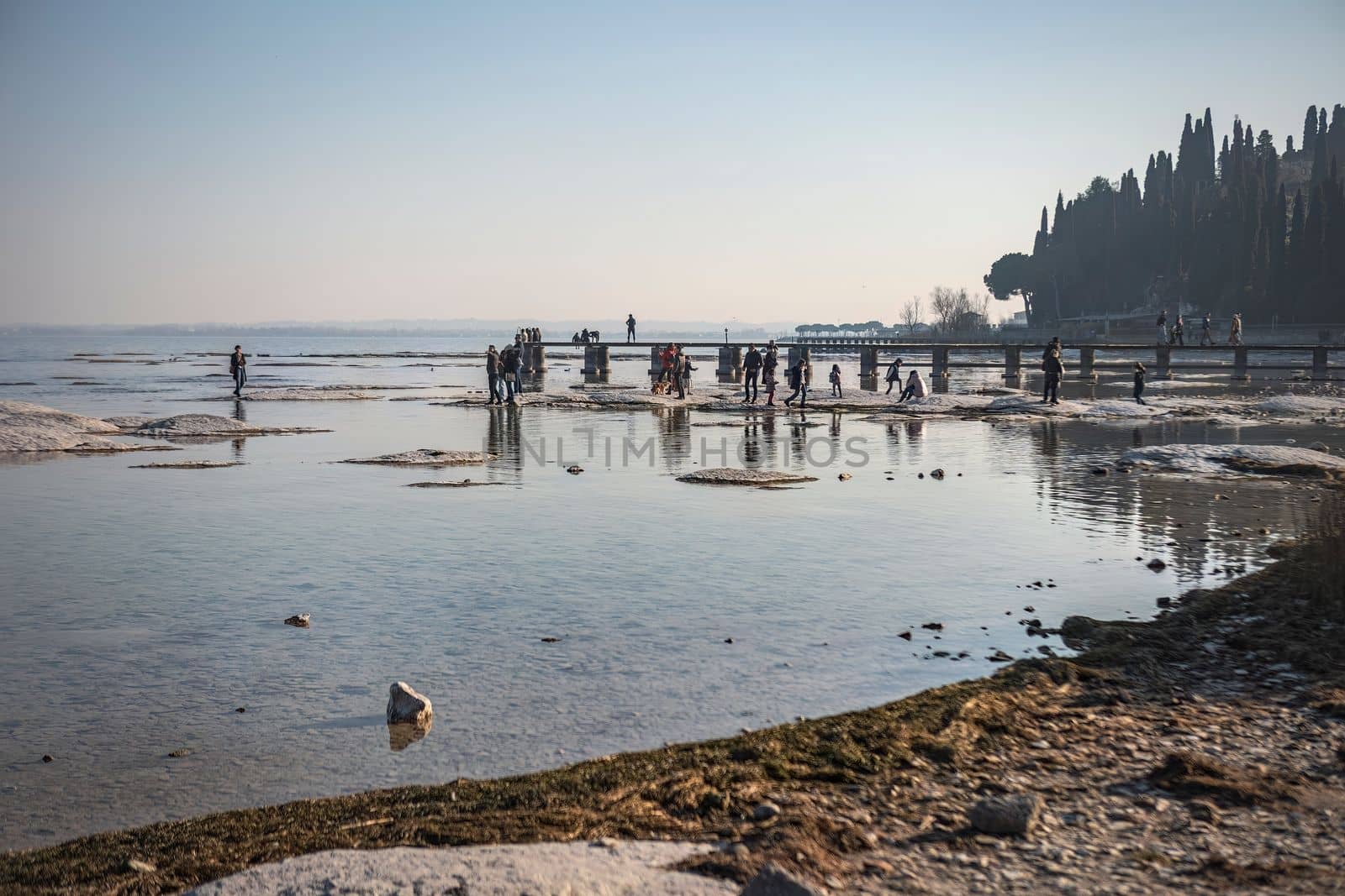 Sirmione, Italy 15 February 2023: A stunning landscape photo of a rocky beach in Sirmione, with the clear waters of Lake Garda in the background