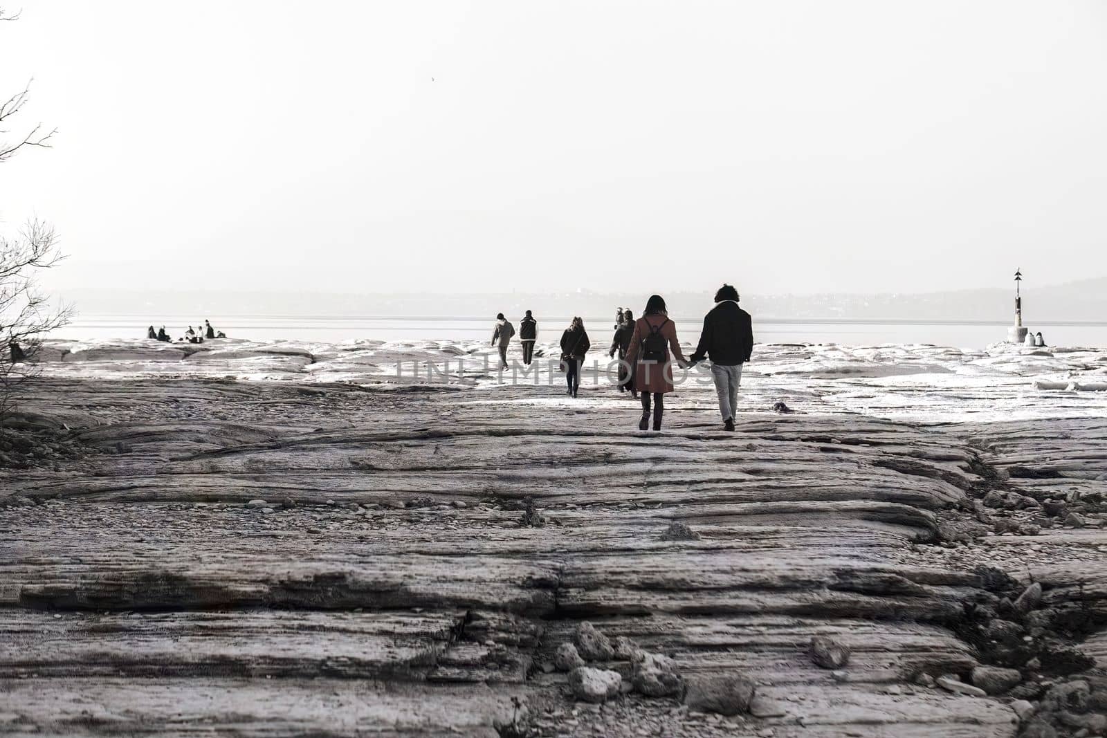 Dreamy Nostalgia: People Walking on Rocky Shoreline in Black and White by pippocarlot