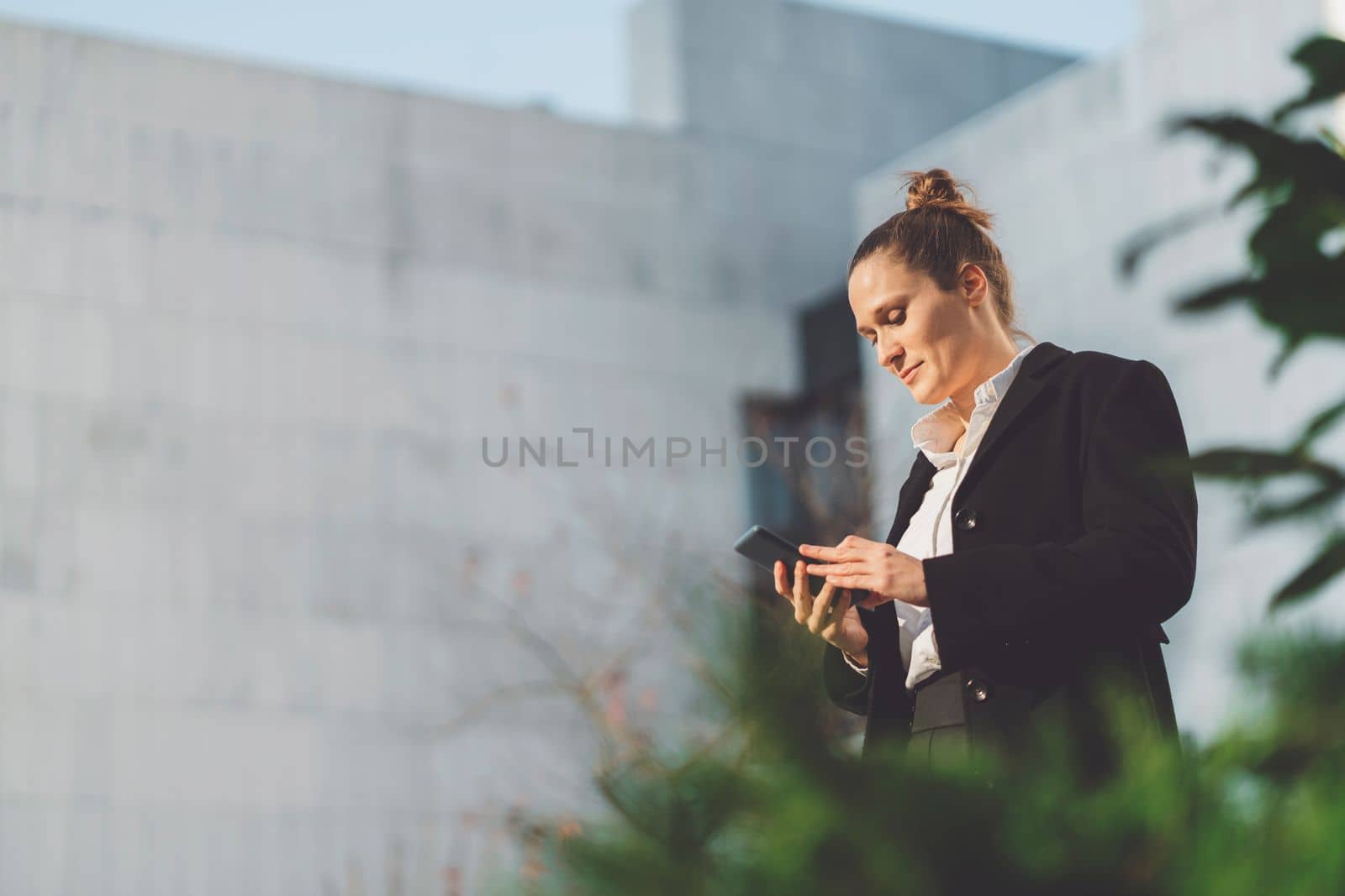 Low angle view, waist up business woman looking down at her phone while walking outside on the sun by VisualProductions