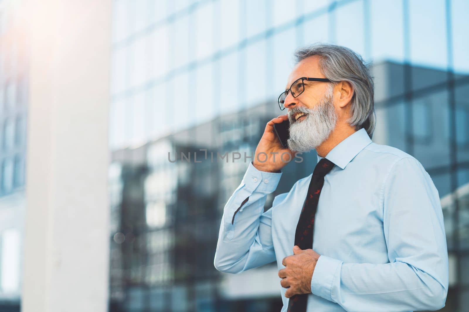 Side portrait of senior businessman talking on the phone outdoors in front of his office building by VisualProductions