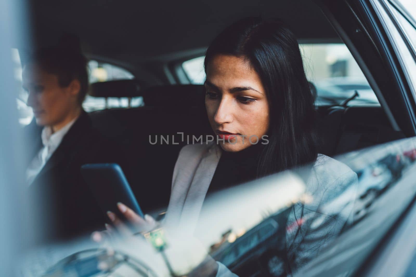 Two business women sitting in the back of a car, focus on one woman looking out the window while on a phone call.