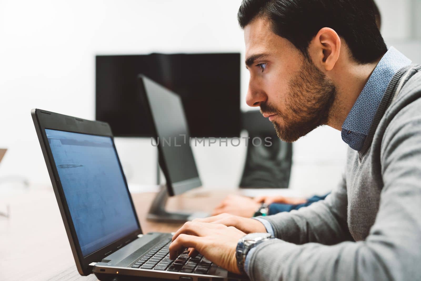 Side view of a focused business man leaning in closer to the laptop screen, coding by VisualProductions