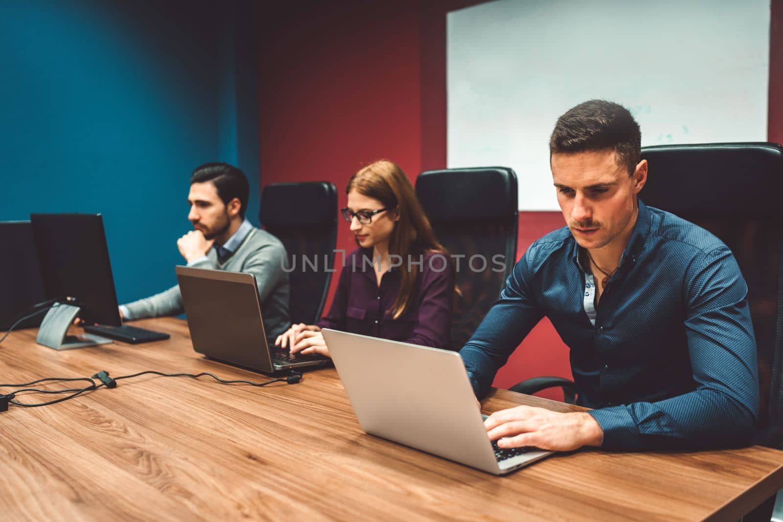 Colleagues at a start up company working on their laptops in colorful red and blue walls in the office by VisualProductions