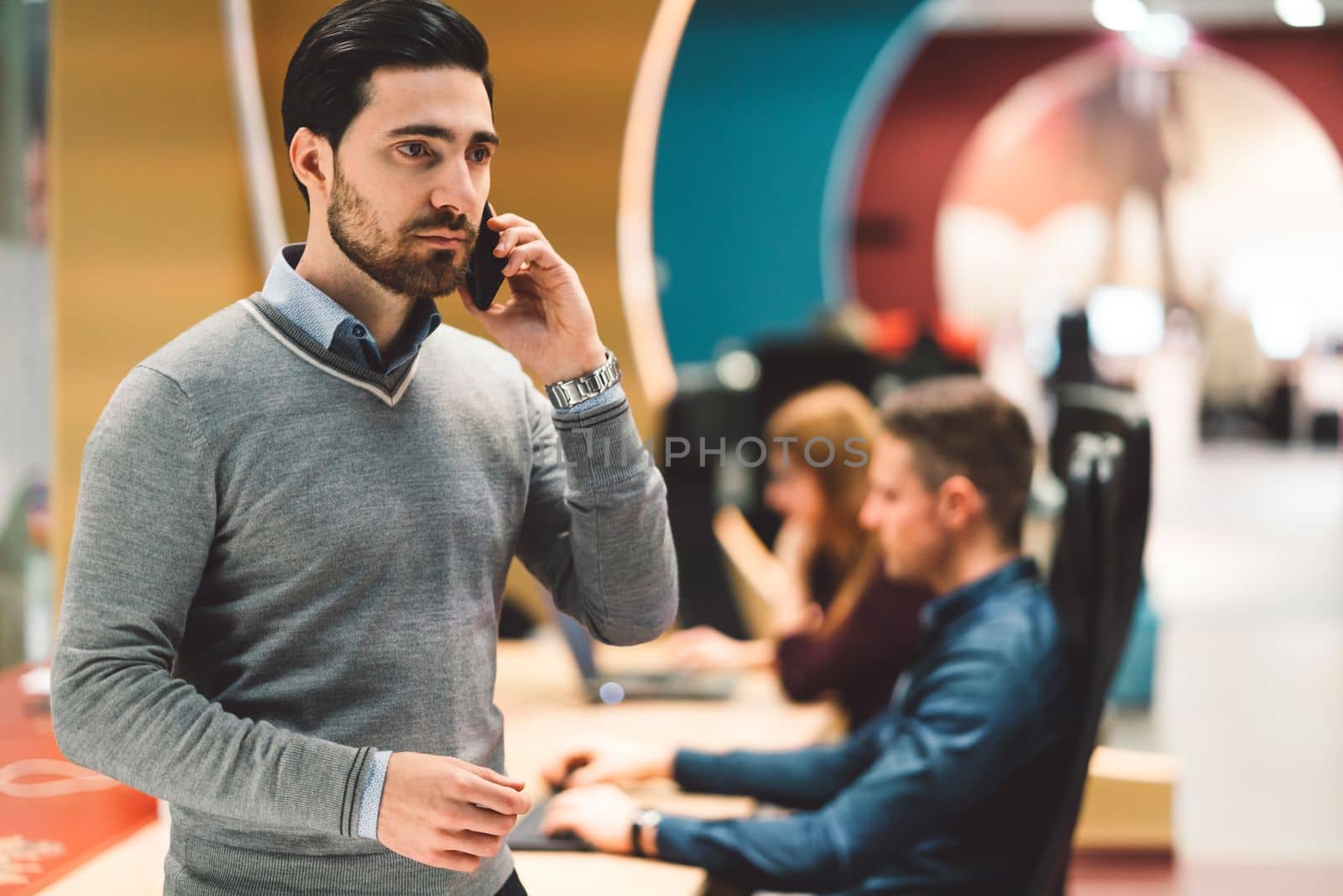 Businessman talking on the phone, while at the office, trying not to disturb his colleagues working next to him by VisualProductions