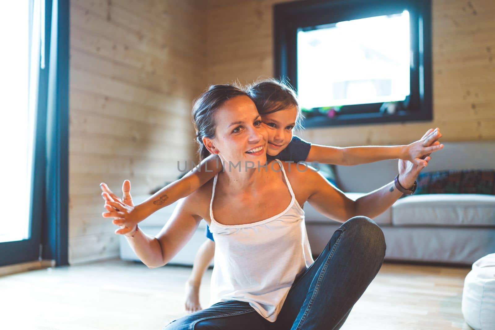 Young girl hugging her mom from behind, playing together on the floor in the living room by VisualProductions