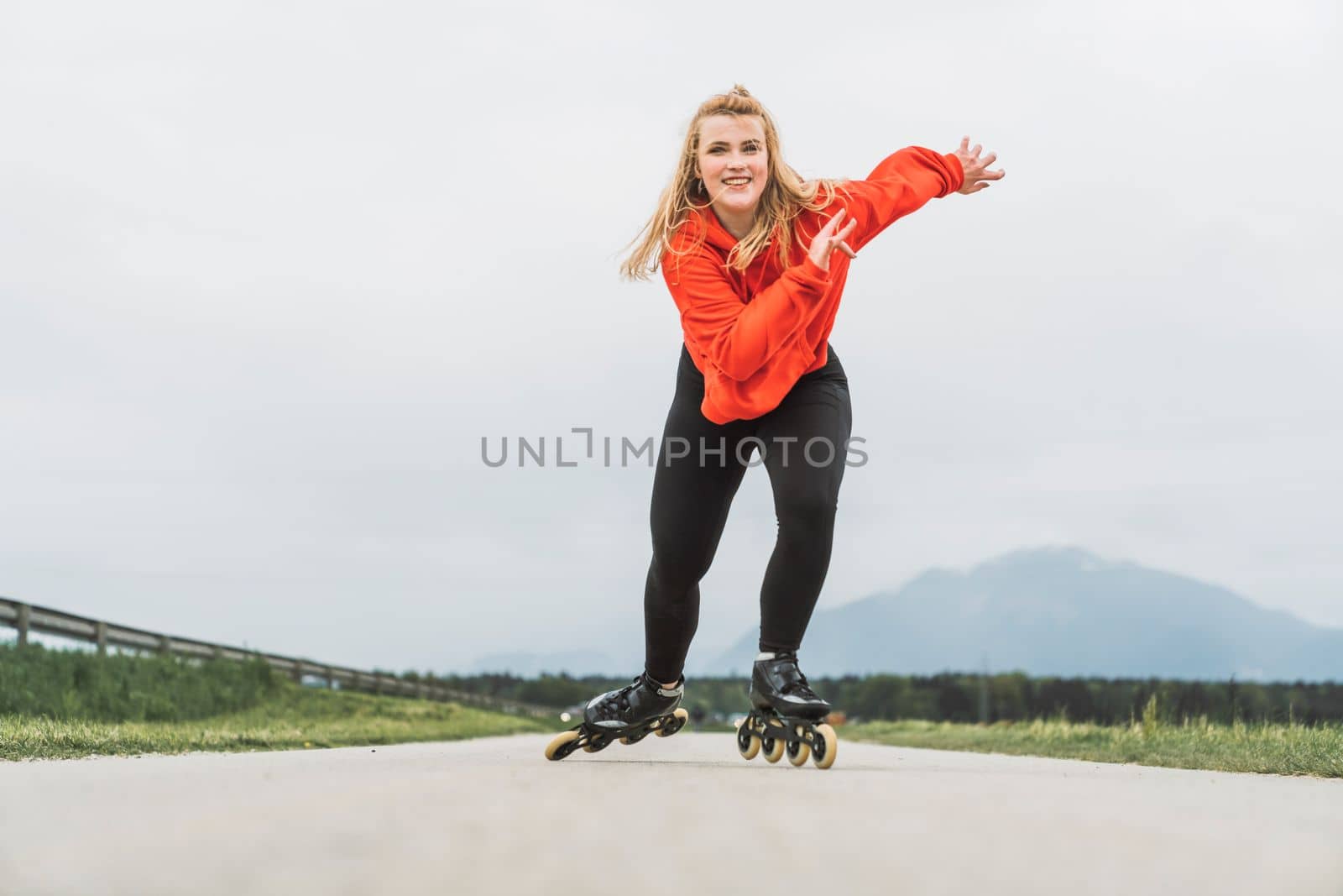View from the front young woman in red jacket skating fast towards the camera with a big smile on her face by VisualProductions