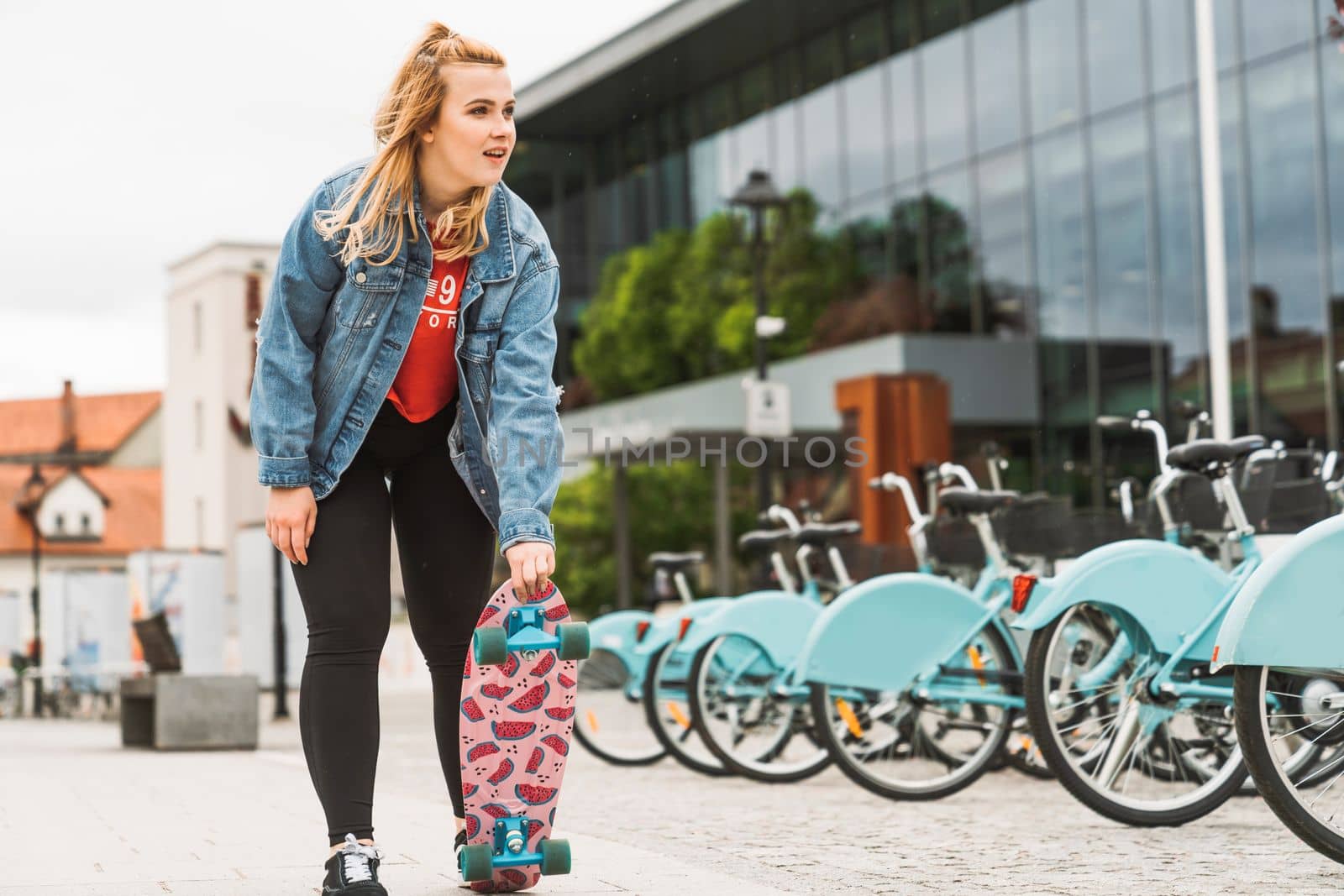 Young blonde caucasian girl having fun outside on a skateboard, wearing black leggings and red shirt, sun flare. Teen girl laughing, having fun outside in the summer.