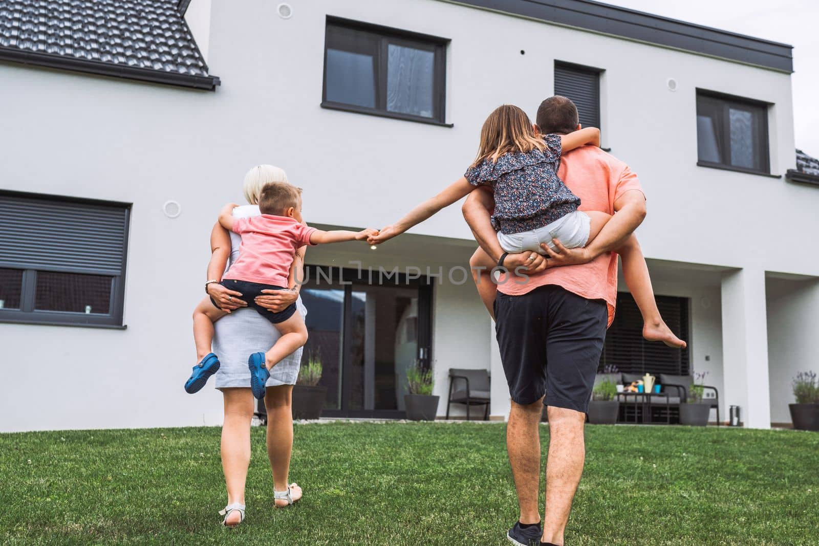 Kids holding hands while their parents carry them on their back - View from behind, house in the background by VisualProductions
