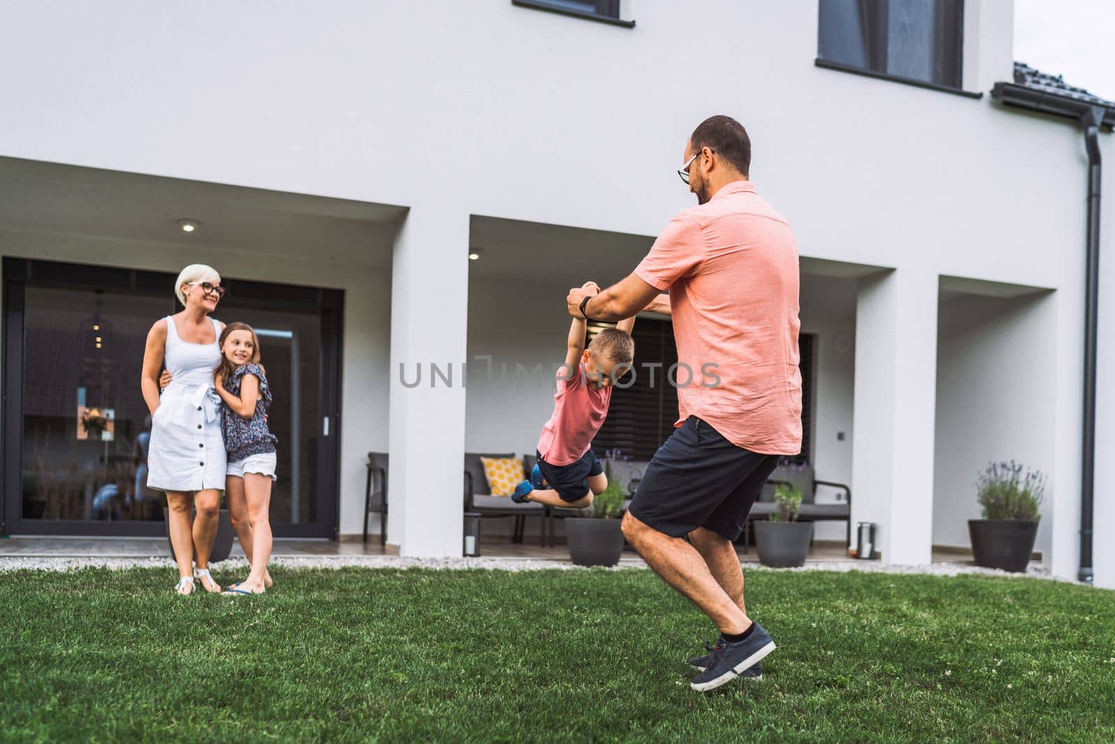 Happy caucasian family of four, mother father and children at home, outdoors playing on the grass, and indoors in the living room having fun as a family.