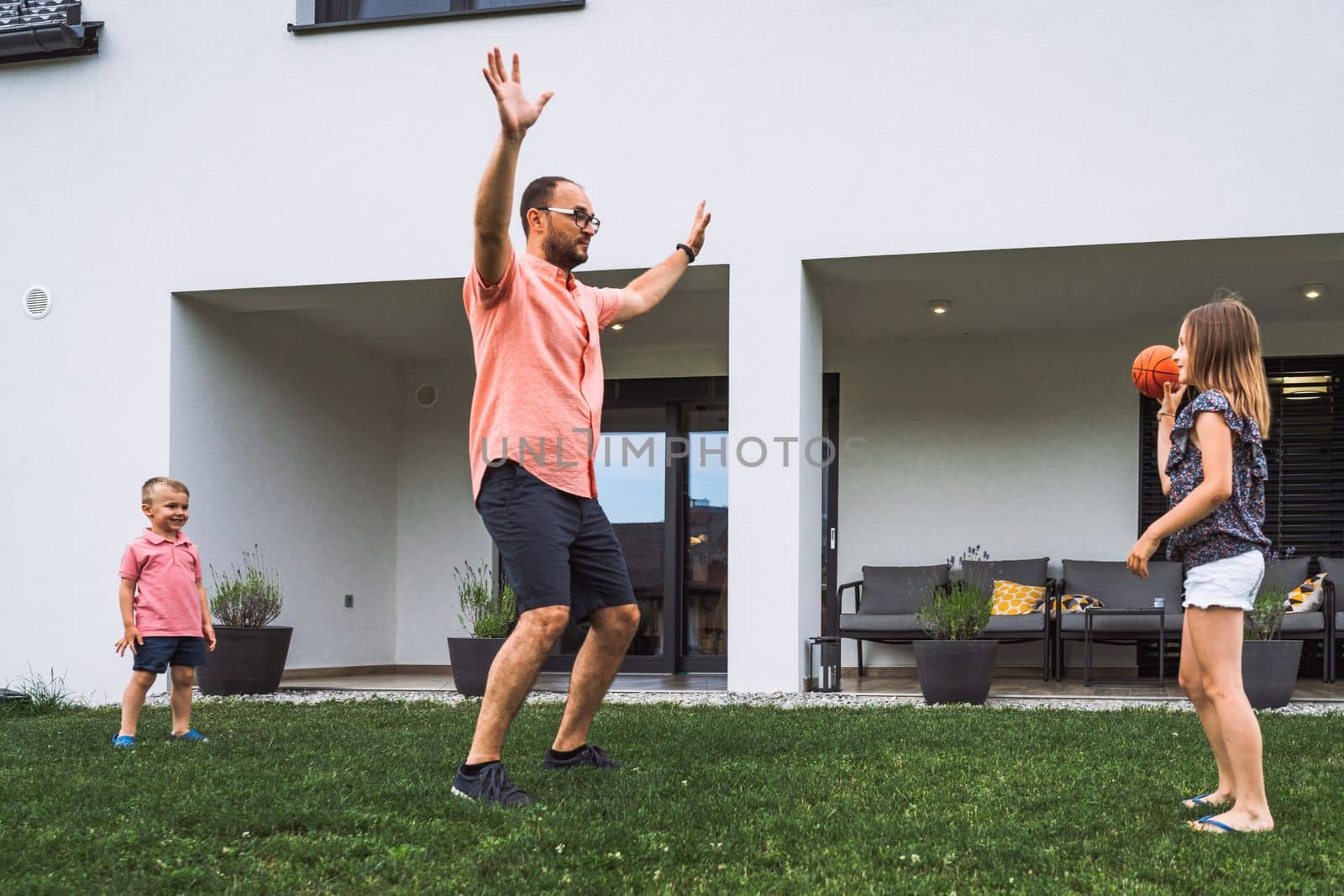 Dad playing games with his two children outside, jumping on the grass having fun by VisualProductions