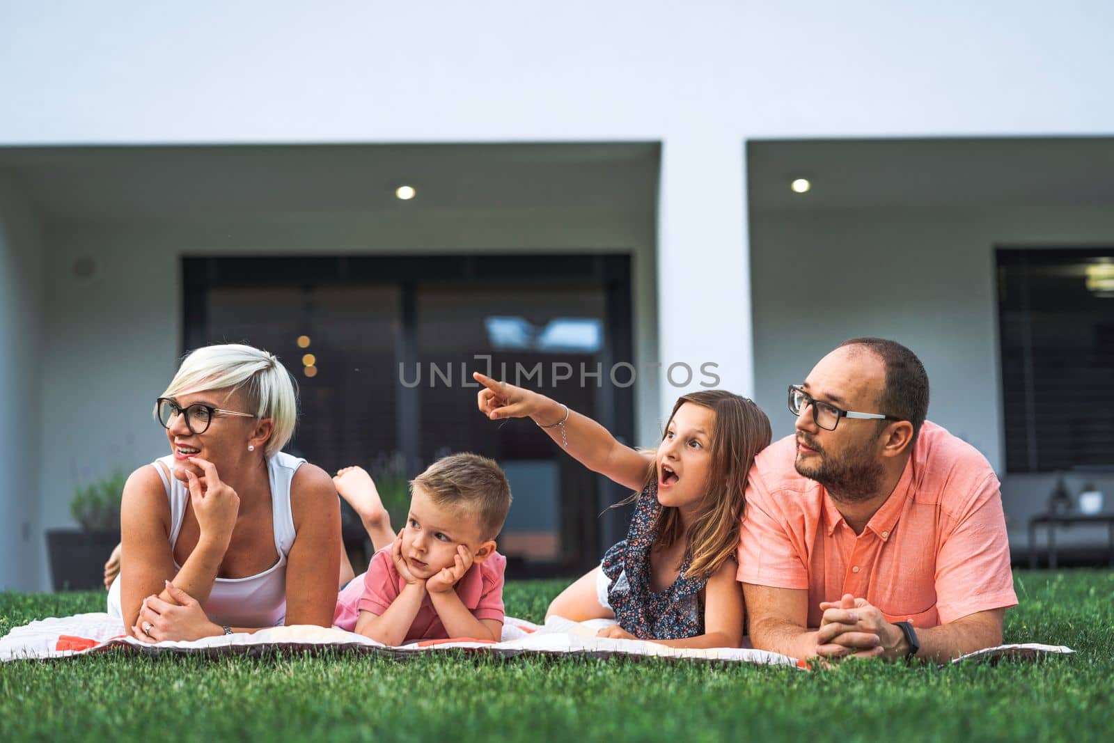 Young family of four laying down on the picnic blanket all of them looking at the same direction by VisualProductions