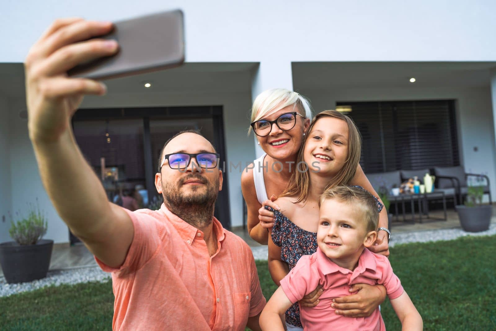 Father holding a phone high up, taking a selfie of the whole family goofing around him by VisualProductions