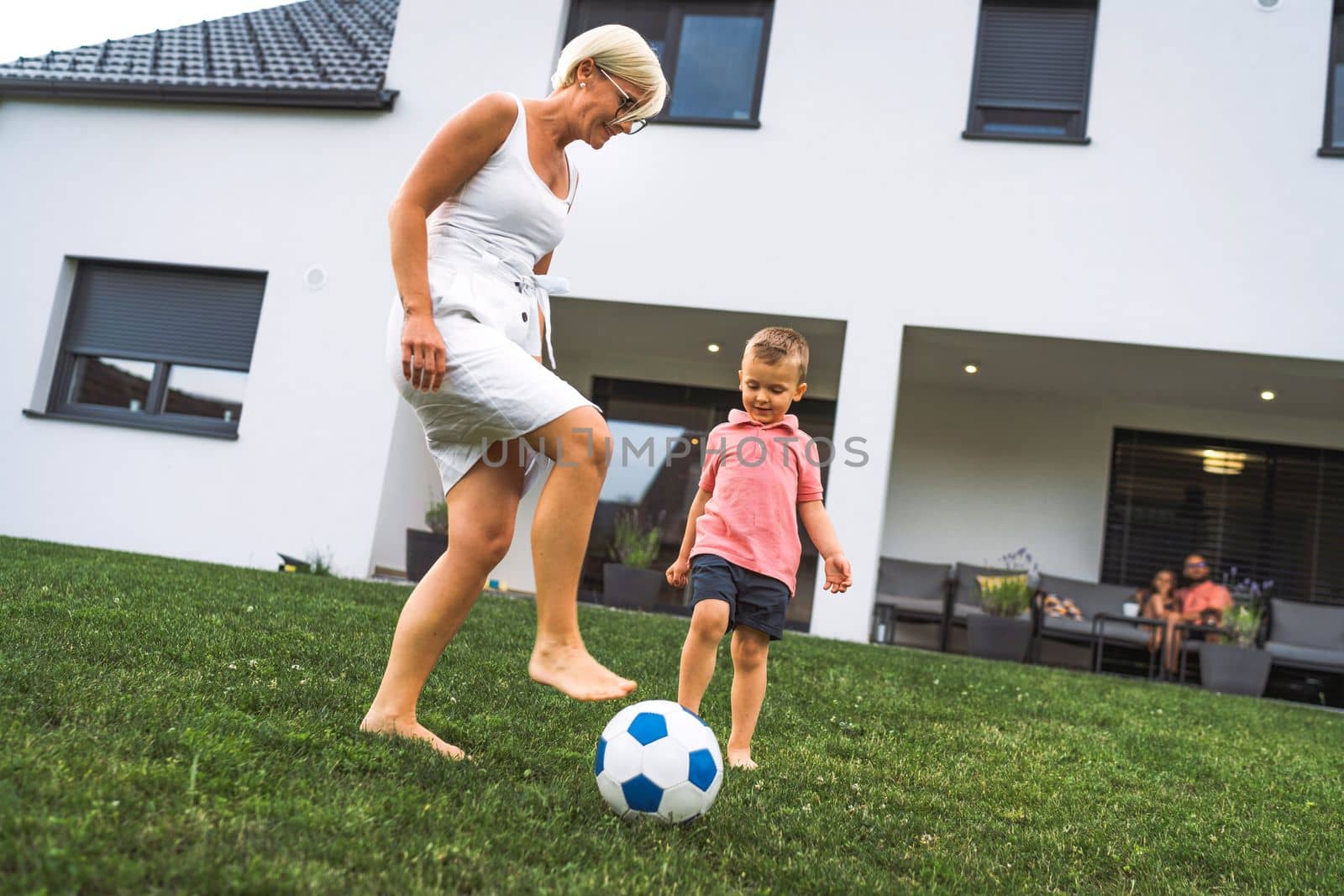 Mom playing football with her son outside the house on the grass by VisualProductions