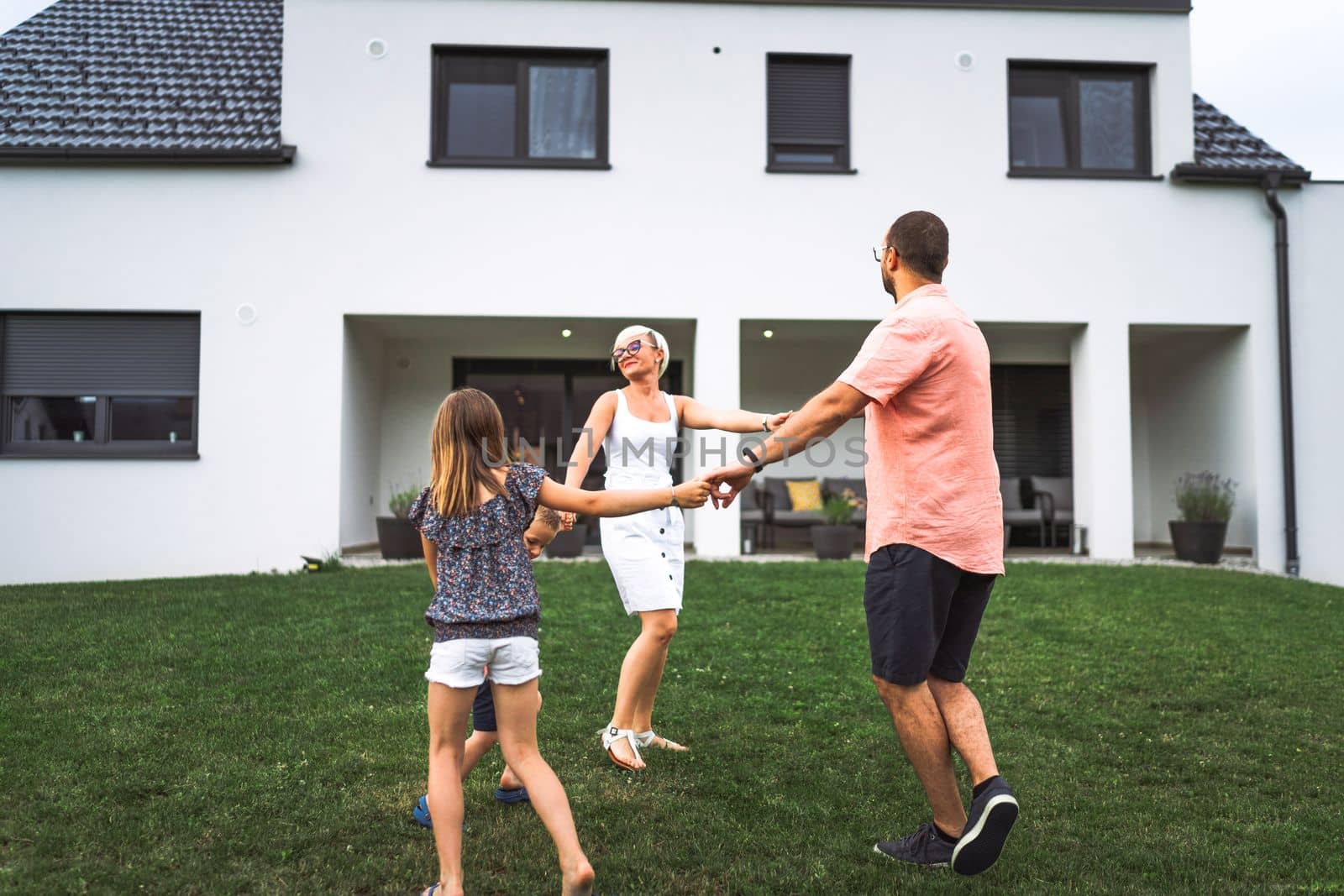 Family dancing together on the grass outside in circle, their new built house in the background by VisualProductions