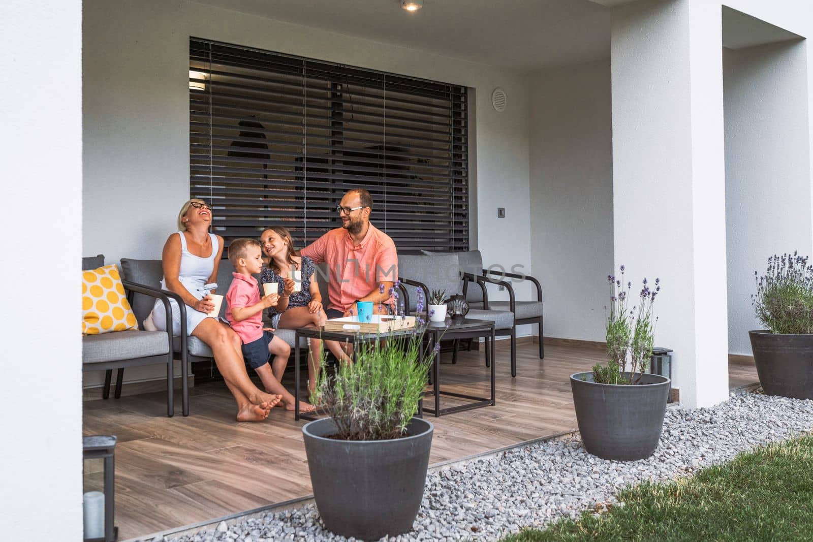 Family sitting outside their house on a nice terrace in the shade, having a drink on a hot summer day by VisualProductions