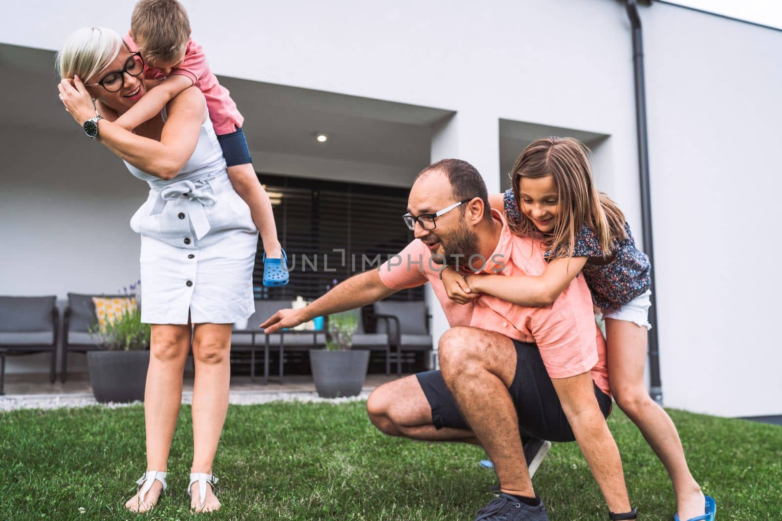 Happy caucasian family of four, mother father and children at home, outdoors playing on the grass, and indoors in the living room having fun as a family.