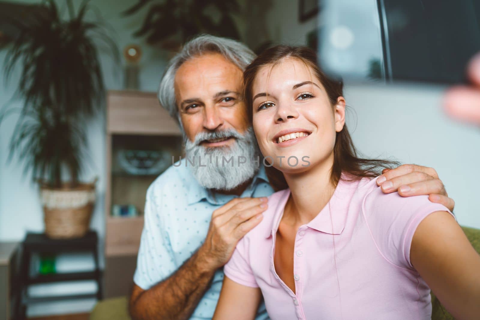 Smiling young woman and senior man her grandfather taking a selfie together by VisualProductions