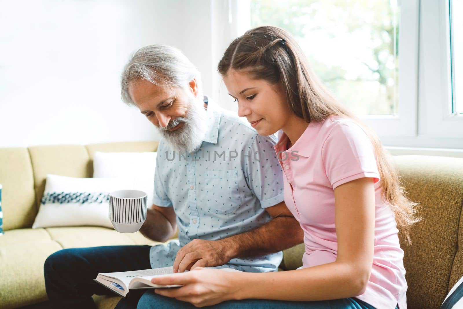 Young caucasian woman taking care of her grandfather, senior man with beard and grey hair. Granddaughter visiting her grandfather, spending quality time together.