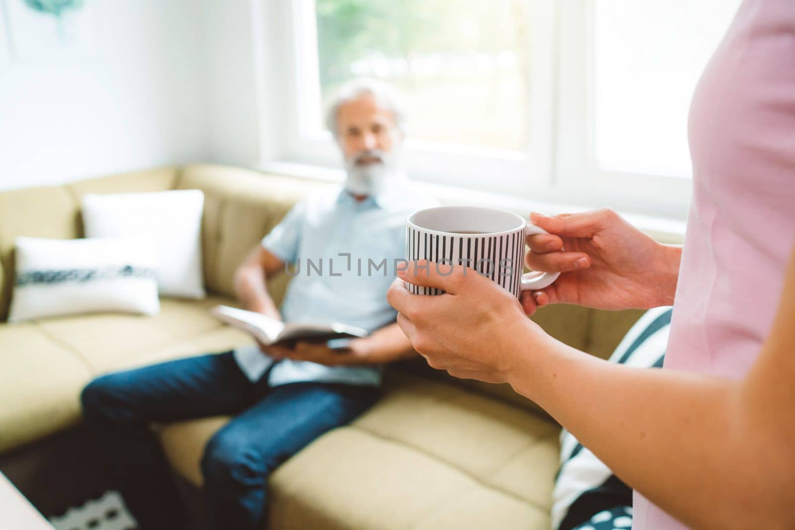 Young caucasian woman taking care of her grandfather, senior man with beard and grey hair. Granddaughter visiting her grandfather, spending quality time together.