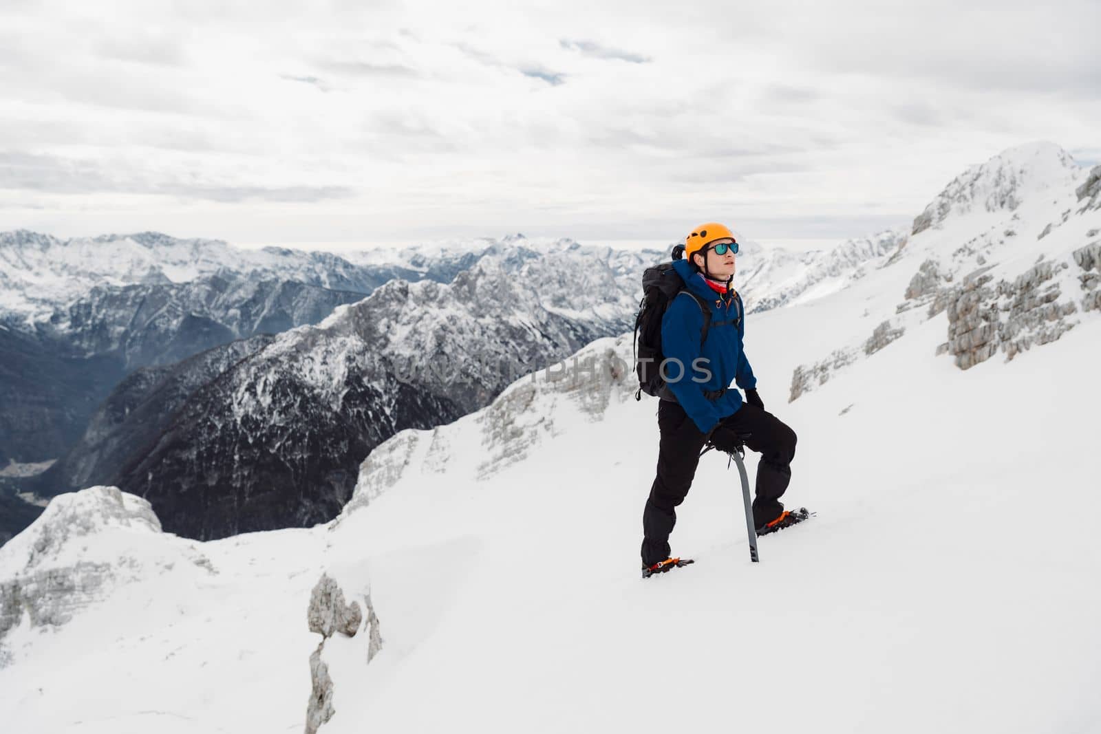Hiker wearing a protective helmet and sunglasses looking up while on a hike up the snowy mountain by VisualProductions
