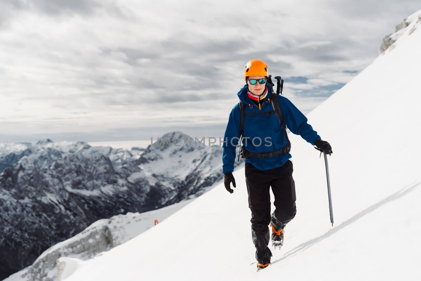 Portrait of a mountaineer with a protective helmet and sunglasses standing in snow, high up in the mountains by VisualProductions