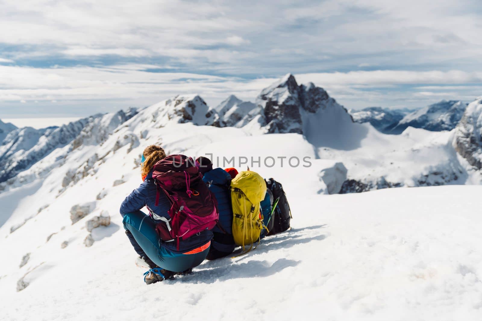 Back view of hiking couple sitting in the snow enjoying the view of winter Alps from high up by VisualProductions